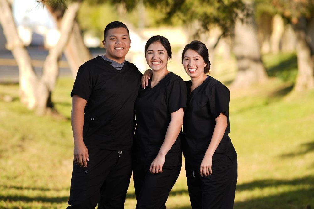 Group of students posing together in scrubs outside of school facility